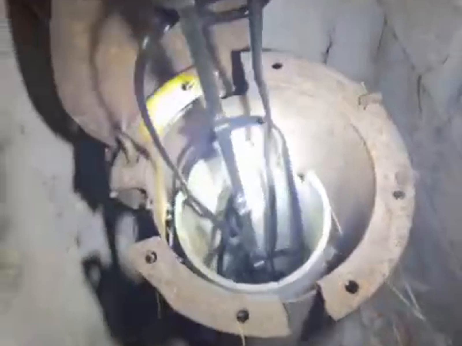 Gece, cıvatalı flanşlı kuyu ağzına tepeden bakış; içeride aşağı inen kablolar ve aydınlatmayla görünen boru cidarı