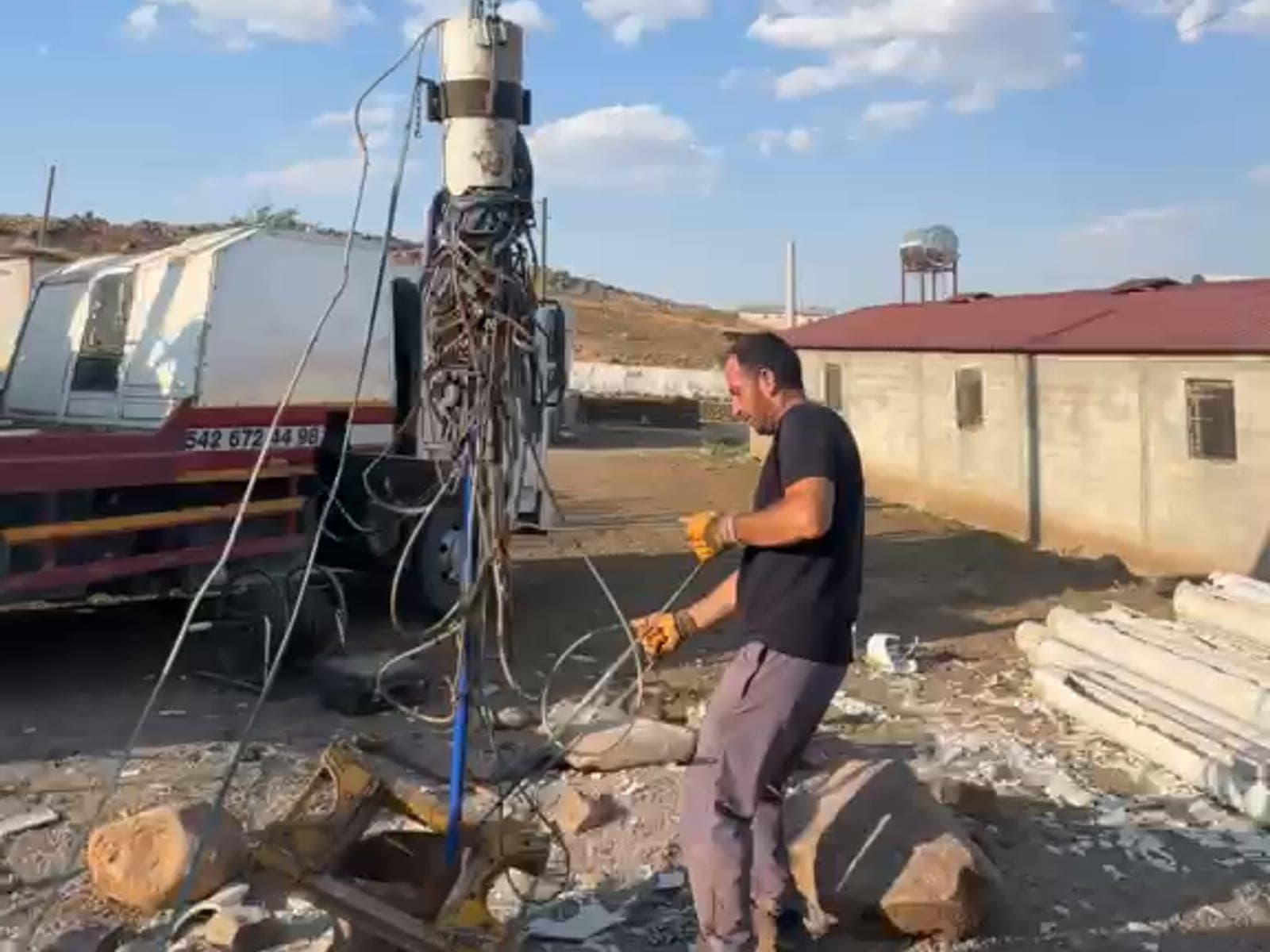 Araç üstü vincin kancasındaki silindirik kurtarma başlığı ve ona dolanmış kablo demeti kuyu ağzının üzerinde asılı duruyor